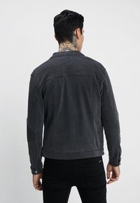 Czarna kurtka dżinsowa o klasycznym kroju, z teksturowanymi prążkami na rękawach oraz subtelnym efektm wyblakłym. Widok z tyłu podkreśla detale szwów.