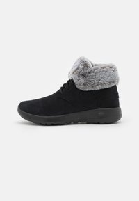 Bottines en daim noir avec un col en fausse fourrure grise, bout rond et semelle en ruban noir. Présente un laçage à l'avant et une texture lisse.