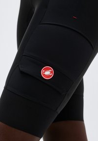 Nahaufnahme von schwarzen Radhosen mit Trägern mit einem roten und weißen Skorpion-Logo auf einer Seitentasche.