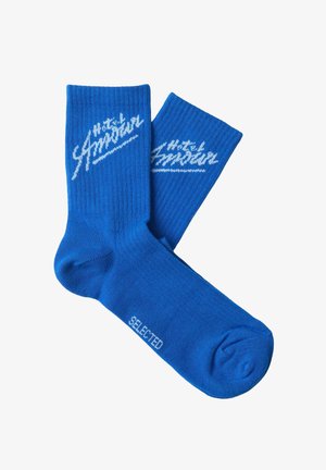 Blå ribbestrikkede sokker med hvit "Hotel Amour"-tekst på mansjettene og "SELECTED"-tekst nær tærne på hvit bakgrunn.