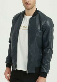 Veste bombardier en cuir bleu marine avec zip à l'avant, col en tricot et poignets. Texture lisse, style ajusté, associée à un t-shirt à col rond blanc.