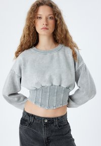 Sudadera gris recortada en tela suave con una cintura acanalada y estructurada, combinada con jeans de mezclilla negros de tiro alto, que cuentan con cierre de botón.