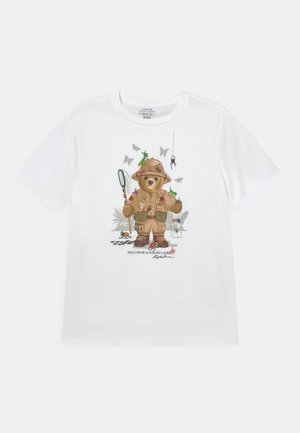 T-shirt en coton blanc avec un ours en dessin animé portant une tenue de safari, tenant un filet, entouré d'insectes et de papillons de différentes couleurs.