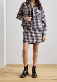 Ensemble de veste et jupe à carreaux en marine et crème, fabriqué en tissu texturé. Comprend une fermeture à boutons, une poche plaquée, et est porté avec des bottines noires à lacets.
