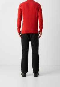 Roter Strickpullover mit hohem Kragen, gerippten B�ündchen und Bund, kombiniert mit schwarzen Jeans mit geradem Bein und schwarzen Schuhen. Einfaches und strukturiertes Design.