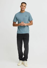 Lyseblåt bomulds t-shirt med korte ærmer og rund hals, prydet med et lille logo på brystet, sammen med sorte lige ben jeans og hvide sneakers.