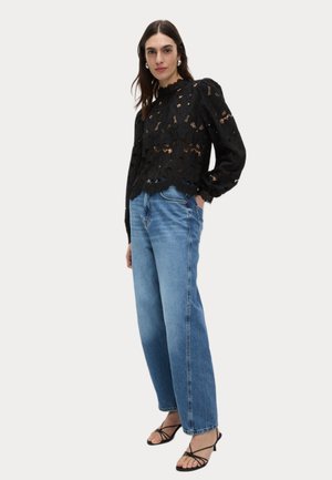 Blusa nera in pizzo con ritagli floreali e scollatura a volant abbinata a jeans azzurri a vita alta e sandali neri con cinturini.