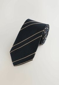 Mørkeblå slips med et struktureret mønster, der har skrå striber i hvid og brun. Rullet design viser den smalere ende.