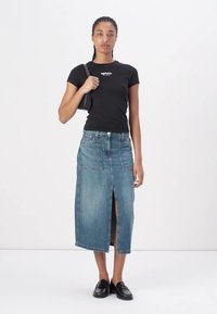 Denim svārki ar vidēji garu piegriezumu līdz tecībai, priekšējo šķēlumu un divām kabatām. Apvienoti ar piegulošu melnu t-kreklu un melnām kurpēm.