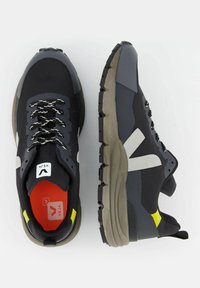 Sneaker in mesh nero con accenti grigi e gialli, caratterizzati da una suola testurizzata, dettagli riflettenti e una soletta rossa a contrasto. Design con lacci.
