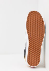 Sneaker sole with a textured rubber design in brown, featuring a white edge. Black upper with yellow and white accents visible on the side.