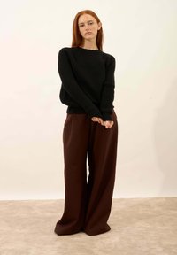 Czarny sweter z dzianiny z okrągłym dekoltem, w połączeniu z brązowymi spodniami o szerokich nogawkach, oba o luźnym kroju i miękkiej fakturze.