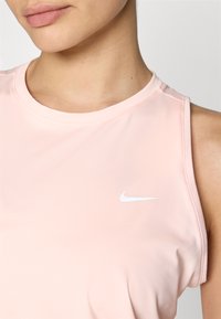 Svijetloružičasti bezrukavni atletski top izrađen od glatke tkanine, sa malim bijelim Nike logom na lijevoj strani grudnog područja.