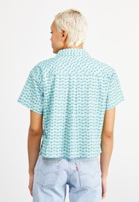 Cămașă cu mânecă scurtă, de culoare albastru deschis, cu un model geometric. Dispune de un guler și un tiv drept, asortată cu blugi din denim deschis.