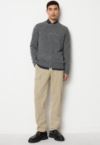 Grauer Strickpullover mit Rundhalsausschnitt; beige Cargo-Hosen mit Taschen; schwarze Slipper; Modell posiert vor einem weißen Hintergrund.