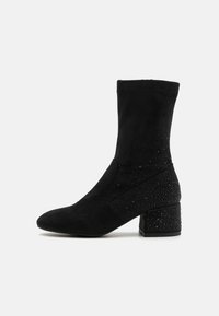 Bottines noires en suède souple avec un talon texturé orné de petites gemmes noires, présentant un design élégant et pointu.