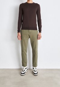 Pull en tricot marron, pantalon vert olive et baskets noires et blanches. Design simple, forme ajustée, poignets côtelés et texture douce.