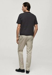 Randig svart och marinblå t-shirt med korta ärmar, i kombination med beiga byxor och svarta skor, sedd bakifrån. Slät tygtextur.