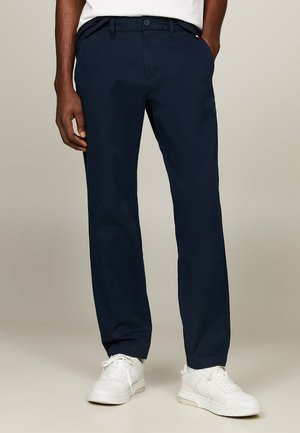 Pantalones chinos azul marino con corte recto, fabricados en un material suave. Presentan trabillas para el cinturón, bolsillos laterales y se combinan con zapatillas blancas.