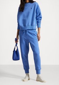 Modrá bavlněná mikina a tepláková souprava s žebrovanými manžetami a stahovacím pasem. Doplněné modrou kabelkou a světlými teniskami.