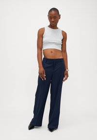 Top cropped cinza, calças largas azul-marinho, tecido suave, design minimalista, com sapatos pretos de bico fino e uma pulseira prateada.