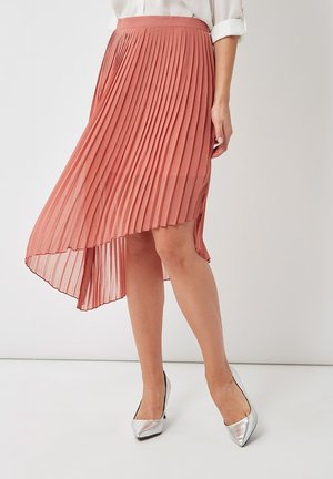 Falda asimétrica plisada en coral con una textura suave, con un dobladillo alto-bajo. Combinada con tacones metálicos plateados de punta puntiaguda.