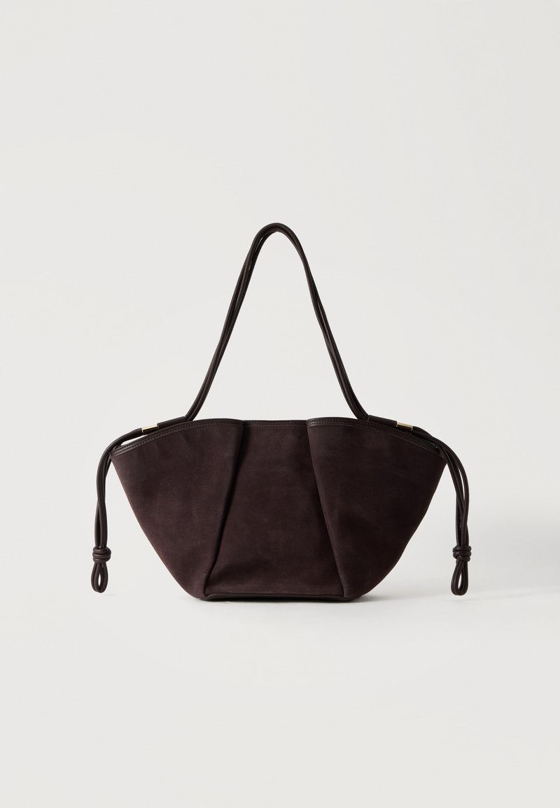 Sac à main en daim marron foncé avec une forme trapèze large, de longues doubles poignées et des détails de cordons noués de chaque côté.