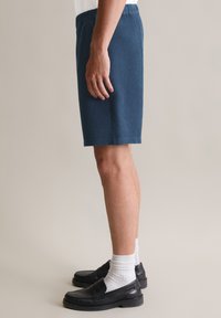 Blauwe shorts met wafelstructuur en een elastische tailleband, die tot halverwege de dij komt. Draag ze met zwarte instappers en witte enkelsokken.
