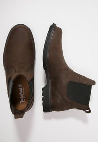 Brown leather ankle boots with elastic side panels, cushioned insole, and a textured rubber sole for grip. Timberland Earthkeepers branding visible.