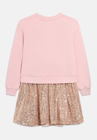 Gaiši rozā krekliņš ar garām piedurknēm un pievienotu spīdīgu rožainā zelta spīguļu svārku, attēlots no aizmugures uz balta fona.