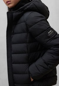 Czarna kurtka puchowa z kapturem, z pikowanym wzorem, zapięciem na zamek oraz naszywką z logo na rękawie. Gładki, ocieplany materiał.