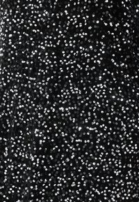 Fekete flitteres szövet sűrű mintázatban elhelyezett, fényes, kerek flitterekkel, amelyek visszaverik a fényt, és texturált, csillogó felületet hoznak létre.