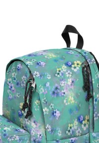 Mochila con un patrón floral en tonos de verde azulado y púrpura. Cuenta con detalles en negro, correas ajustables y un asa superior para llevarla.