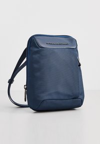 Borsa a tracolla blu navy realizzata in tessuto texturizzato, con chiusura zip e logo. Cinturino regolabile e forma rettangolare compatta.