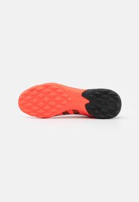 Suola di scarpa da calcio con una sezione in gomma nera testurizzata e una parte arancione brillante con un motivo geometrico.