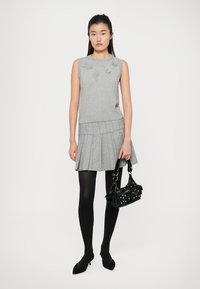 Maglione grigio senza maniche con dettagli floreali texture, abbinato a una gonna grigia a pieghe, collant neri e una borsa nera con borchie.