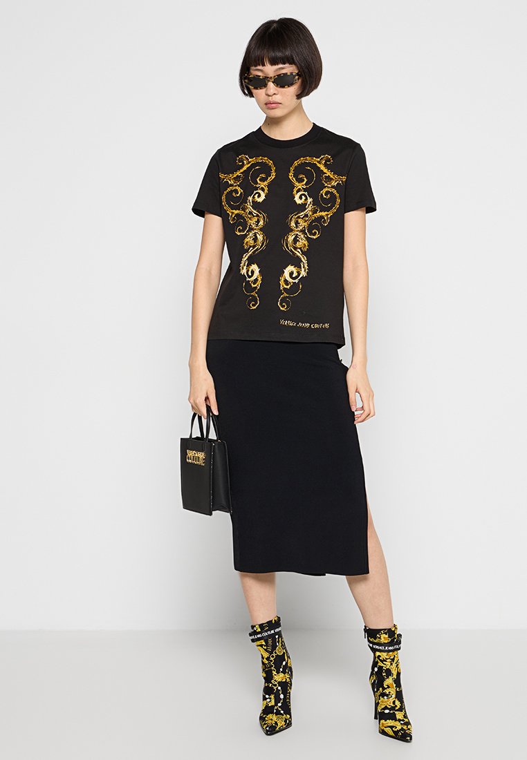T-shirt noir avec un motif tourbillonnant doré, associé à une jupe midi noire, des bottes ornées d'un imprimé chaîne doré et un petit sac à main noir.