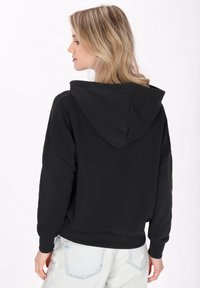 Hanorac negru din material moale, cu o croială lejeră, având o glugă mare și manșete ribbate. Asortat cu blugi de culoare albastru deschis.