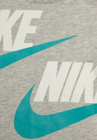 Gray cotton t-shirt featuring large white "NIKE" text and a turquoise Nike swoosh graphic. Smooth texture, casual design.