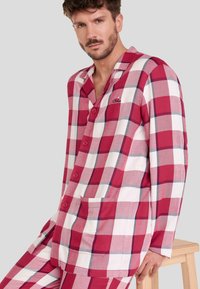 Conjunto de pijama a cuadros rojos y blancos hecho de algodón suave. Incluye una camisa con botones y un bolsillo, y pantalones a juego.