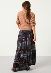 Pudergrauer, kabelgestrickter Pullover mit kurzen Ärmeln, kombiniert mit einem langen, gemusterten Rock in dunklen Farben mit geometrischen Designs und einem ausgestellten Saum.