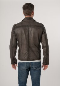 Giacca di pelle marrone da uomo con una texture liscia, taglio dritto e dettagli di cucitura minimi, abbinata a jeans blu.