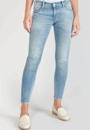 Skinny jeans in light blue denim, featuring a faded wash, distressed details, and classic five-pocket design. Paired with cream loafers.