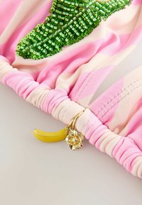 Tissu rayé rose et crème avec détail de feuille perlée verte et petits charms dorés en forme de banane jaune et de fleur.