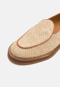 Vevevd beige loafers med lærbeslag, stablet søm og brun såle, vist i nærbilde på hvit bakgrunn.
