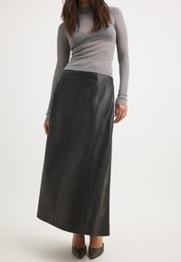 Gonna maxi nera in pelle con una texture liscia e dettagli di cuciture verticali, abbinata a un top fitted grigio a maniche lunghe con costine.