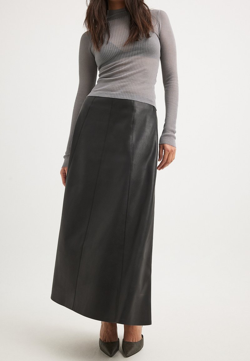 Gonna maxi nera in pelle con una texture liscia e dettagli di cuciture verticali, abbinata a un top fitted grigio a maniche lunghe con costine.