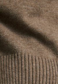 Brązowa dziana tkanina, charakteryzująca się gładką teksturą i pionowym prążkowanym wzorem, z delikatnymi wariacjami w kolorze i miękkości.