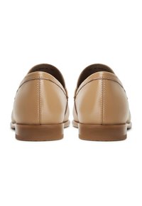 Scarpe in pelle marrone chiaro con una texture liscia, forma arrotondata e piccoli tacchi marroni. È visibile un dettaglio di cucitura lungo le cuciture.