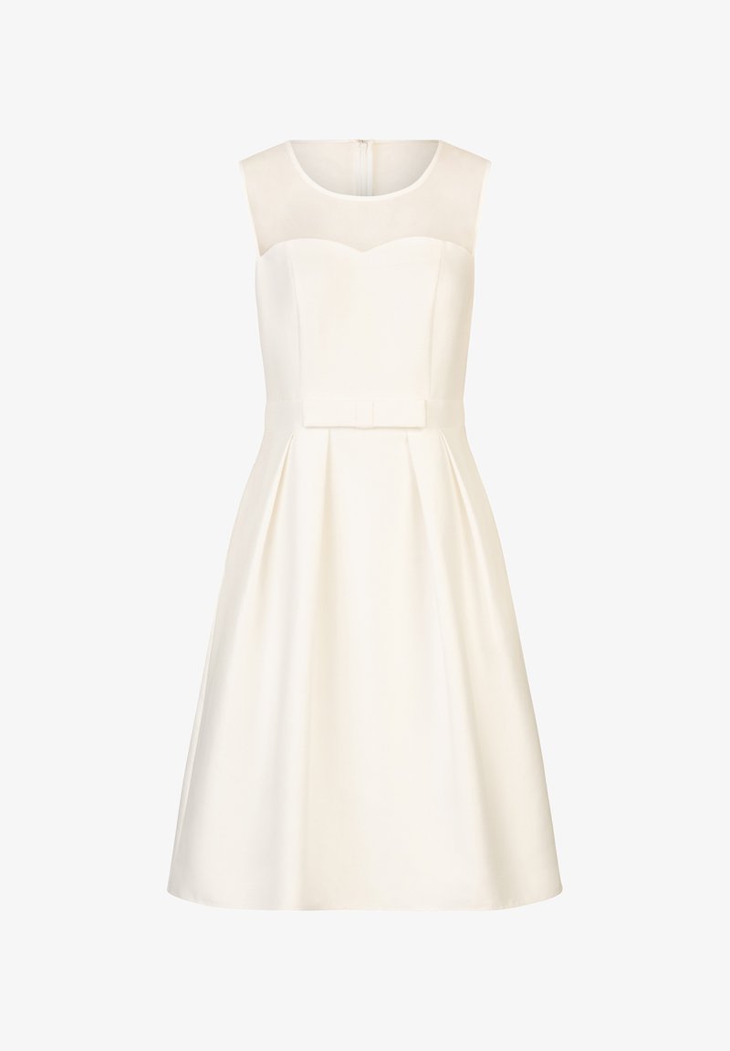 Robe blanche sans manches longueur genou avec encolure transparente, corsage ajusté et jupe plissée avec un petit nœud en tissu à la taille.